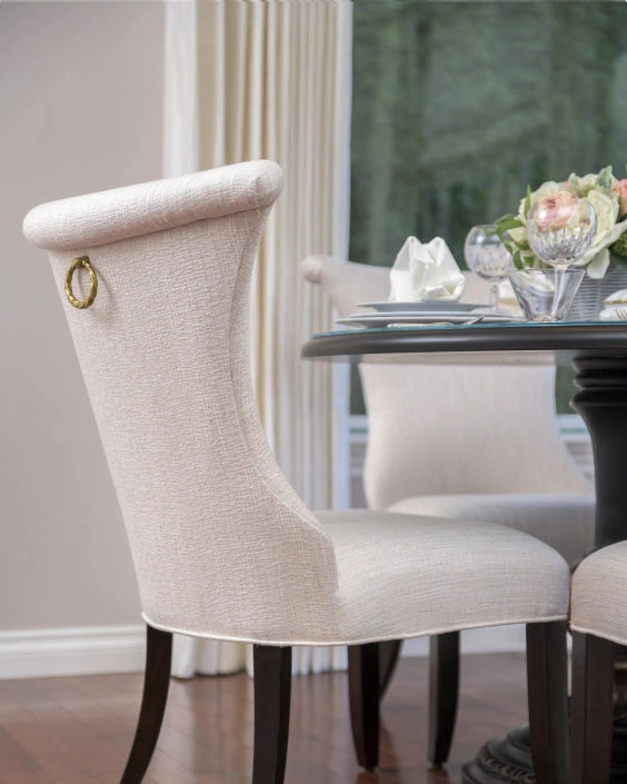 Beige upholstered chair with a gold ring detail in a dining room setting.