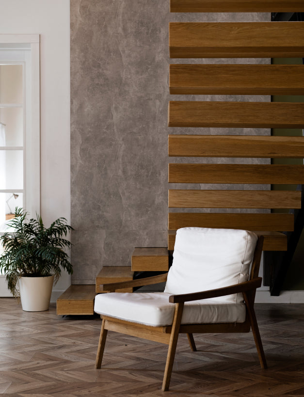Wooden armchair with white cushion in a room with a textured wall and wooden floor.